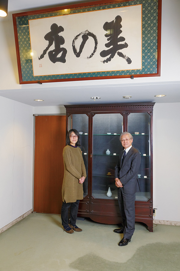 澤田瞳子さんと壺中居代表取締役の松浪幸夫さん 2020 年３月壺中居にて。扁額は川端康成氏の揮毫。 （目の眼2020 年6 月号連載「美の仕事」）